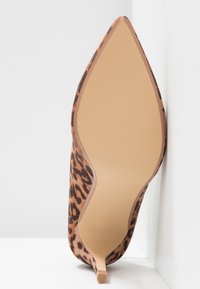 Chaussure à talon kitten à bout pointu avec dessus imprimé léopard et semelle beige lisse, présentée en angle sur fond blanc.