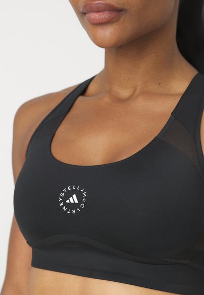 Sostenedor deportivo negro hecho de tela suave con acentos de malla. Presenta un logo blanco redondo en el centro y un escote redondeado para mayor comodidad.