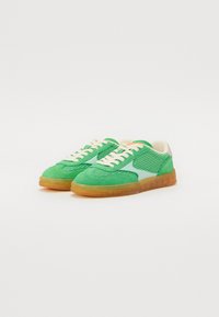 Grønne sneakers med mesh og ruskind, kremfargede lissser og en gjennomsiktig gummisåle. Har et lyseblått akcent på siden.