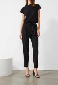 Haut noir à manches courtes avec encolure ronde, associé à un pantalon noir taille haute doté d'une ceinture en tissu et de jambes fuselées et droites.