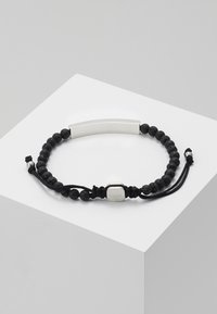 Pulsera de cuentas de piedra de lava negra con un centro de barra de plata, cordón ajustable y cierre de plata grabada. Diseño simple con texturas contrastantes.