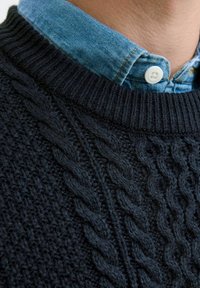 Pull en maille bleu marine avec un motif de cable texturé, featuring un col rond côtelé. Col de chemise en denim bleu clair visible en dessous.