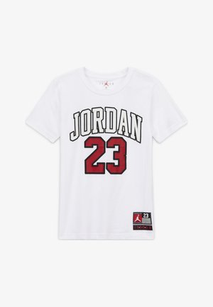 Bijela pamučna majica kratkih rukava s natpisom "JORDAN" u crnoj i crvenoj boji, brojem "23" u crvenoj boji i crnom oznakom u donjem desnom kutu s detaljima logotipa.