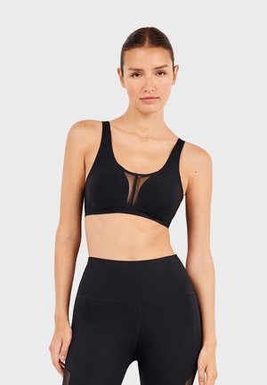 Black sports bra with wide straps, sheer mesh panel at the front, smooth fabric, and seamless design, paired with black high-waisted leggings.