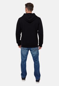 Sudadera negra con cordón y bolsillo tipo canguro, combinada con unos pantalones vaqueros de denim azul claro. La tela parece suave y tiene un corte confortable.