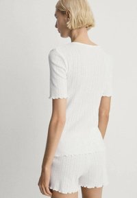 Top a coste bianco a maglia e pantaloni corti abbinati con bordi scallop, caratterizzati da un motivo testurizzato. Progettato con maniche corte e una vestibilità comoda.