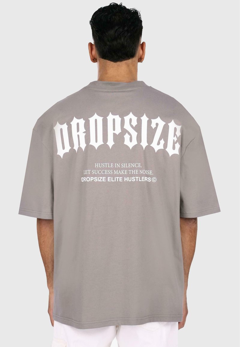 Overdimensioneret grå t-shirt med fed hvid tekst "DROPSIZE" på ryggen. Har en rund halsudskæring og korte ærmer, lavet af blødt bomuldsstof.