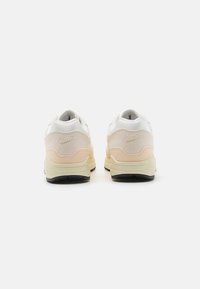 Nike Air sporta apavi ar baltu un gaiši rozā augšdaļu, zamšādas un sieta materiālu, biezu zoli un zīmolu logo iegrieztu papēdī.