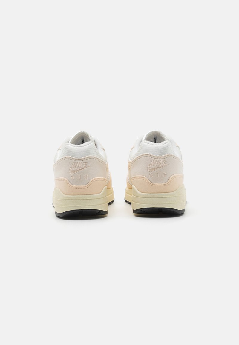 Baskets Nike Air avec un dessus blanc et rose clair, en daim et en mesh, semelle épaisse et logo de la marque embossé au niveau du talon.