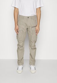 Světlé béžové cargo kalhoty s několika kapsami a boční kapsou na zip, vyrobené z odolného materiálu a s rovným střihem.