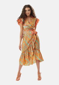 Wrap dress in a colorful plaid pattern featuring orange, turquoise, and yellow. Ruffled sleeves and a tiered hem enhance its flowing design.