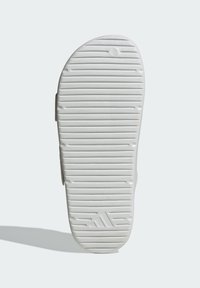 Valkoisen tennarin pohja, jossa on kuvioitu pito, vaakasuuntaiset uurteet ja pienet pyöreät korostukset. Sisältää kohokuvioidun logon.