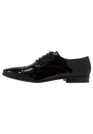 Chaussure de ville formelle en cuir noir brillant avec bout pointu, fermeture à lacets et petit talon empilé, vue de profil latéral.