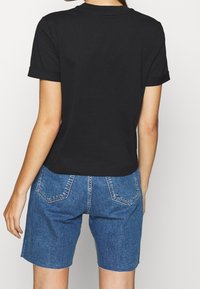 Black cotton t-shirt with short sleeves and a crew neck, paired with blue denim shorts featuring back pockets and a frayed hem.