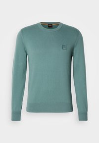 Pull uni à manches longues col rond en teal atténué avec poignets et ourlet côtelés, avec un petit patch carré avec logo sur la poitrine gauche.
