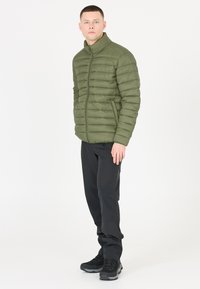 Olivengrøn pufferjakke med stående krave og kviltet design, parret med sorte bukser og sorte fodtøj med grå accenter.