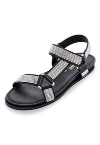 Zwarte sandaal met strass-accenten, verstelbare banden en een platte zool. Beschikt over een glad leren voetbed en metallic hardware-details.