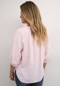 Helle rosa Leinenbluse mit gepufften Ärmeln, rüschigem Ausschnitt und gerafften Manschetten, mit abgerundetem Saum und entspannter Passform.