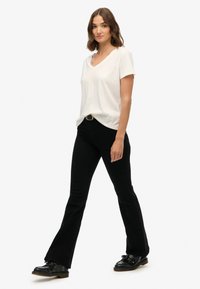 Camiseta blanca de cuello en V hecha de tela suave, combinada con unos jeans negros ajustados y acampanados. El conjunto incluye una hebilla de cinturón dorada y unos zapatos negros.