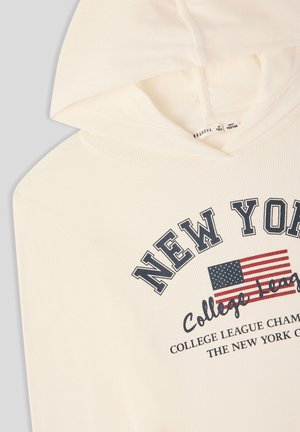 Felpa di colore crema con texture a coste verticali, dotata di testo "NEW YORK" e grafica di una bandiera americana sul davanti. Tessuto morbido, design casual.