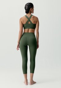 Zelený športový podprsenka má krížové ramienka, hladkú látku a priliehavý dizajn. K tomu dokončujú športový vzhľad zodpovedajúce legíny s vysokým pásom.