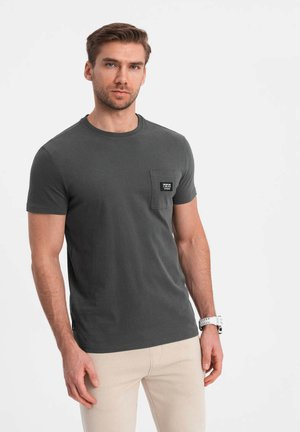 Camiseta de algodón gris con cuello redondo y mangas cortas. Presenta un bolsillo delantero con una etiqueta negra. Textura suave, ajuste casual.