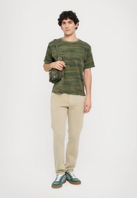 Grön kamouflage t-shirt, beige byxor och gröna sneakers. Inkluderar en liten grön axelväska. Utformad för casual användning.