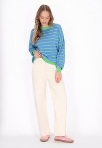 Gestreifter Pullover in Blau und Grün mit grünem Kragen, kombiniert mit cremefarbenen, weit geschnittenen Hosen und rosa Sneakers.