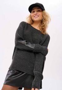 Grauer gestrickter Pullover mit schwarzen Kunstlederakzenten an den Ärmeln, verfügt über einen gerippten Saum und ein übergroßes Design, kombiniert mit einem schwarzen Leder-Minikleid.
