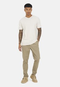 Kremowa koszulka polo z teksturowanym wzorem, zestawiona z beżowymi spodniami i jasnymi butami z detalem w postaci klamry.