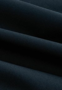 Zwarte stof met een gladde, matte textuur, voorzien van gevouwen lagen die zachte schaduwen creëren. Geen zichtbare patronen of hardware.