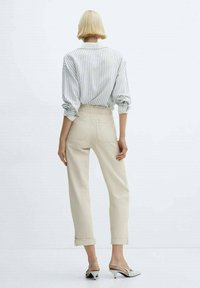 Blusa bianca a righe con maniche a sbuffo, abbinata a pantaloni beige chiaro a vita alta. Include polsini arrotolati e scarpe con punta aperta.