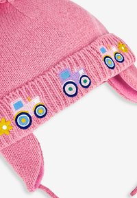 Gorro de punto rosa con orejeras, que presenta tractores bordados en azul, amarillo y rosa en el ala, y un pompón esponjoso en la parte superior.