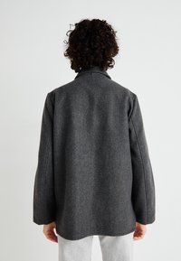 Cappotto grigio in misto lana con una vestibilità morbida, dettagli di cucitura visibili e colletto. La schiena presenta una texture liscia e un orlo dritto.