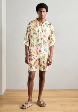 Set leggero composto da una maglietta a maniche corte e pantaloni corti in colori pastello con motivi tropicali. Realizzato in tessuto traspirante, adatto per il clima caldo.