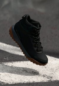 Czarne buty trekkingowe Columbia z teksturowaną cholewką, okrągłymi sznurówkami i trwałą gumową podeszwą w kolorze pomarańczowo-brązowym. Posiadają wzmocnienie wokół kostki.