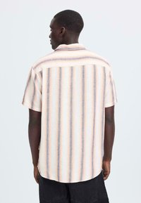 Korte mouw blouse van lichte stof met verticale strepen in pastelkleuren. Voorzien van een rechte zoom en een detail van de achterpas.