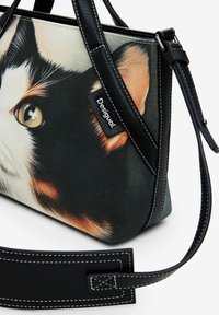 Borsa nera e beige con una stampa di gatti dettagliata. Realizzata in tessuto con accenti in pelle nera, presenta un manico corto e una tracolla regolabile.