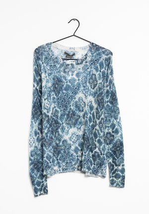 Blå og hvid strikket trøje med lange ærmer og abstrakt blomstret og geometrisk mønster, hængende på en sort bøjle mod hvid baggrund.