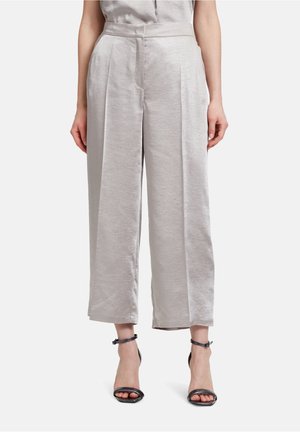 Pantalons larges gris clair en tissu lisse, dotés d'une taille haute et d'un détail plissé à l'avant. Associés à des talons noirs à lanières.