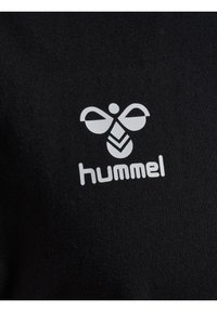 Svart tyg med en slät textur har en vit Hummel-logotyp som föreställer en abstrakt bi-design ovanför varumärkesnamnet i små bokstäver.