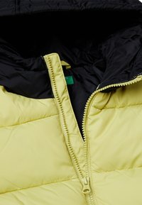 Giacca imbottita con esterno giallo e fodera interna nera, chiusura con zip e cuciture tono su tono. Tessuto liscio con motivo trapuntato.