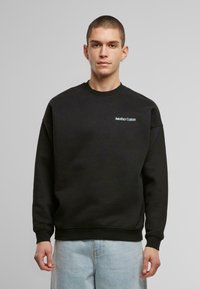 Sudadera negra de algodón con cuello redondo y puños acanalados. Presenta un pequeño logotipo en blanco de "Another Cotton" en el lado izquierdo del pecho.
