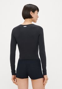 Haut noir à manches longues, coupe ajustée, matière en coton lisse. Doté d'un col rond et d'une étiquette à l'arrière. Assorti à un short foncé.