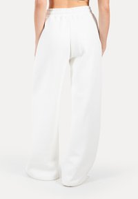 Pantaloni tuta bianchi, dal taglio comodo, realizzati in un tessuto morbido, con una vita elastica e gambe ampie dallo stile pulito e minimal.