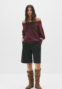 Bordeaux off-shoulder trui, zwarte op maat gemaakte shorts en tan slouchy kniehoge laarzen; heeft een ontspannen pasvorm en een gestructureerde stof.