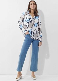 Langärmlige, gemusterte Bluse in Creme, Blau und Marineblau. Kombiniert mit hellblauen schmalen Jeans und weißen Loafers mit goldenen Akzenten.