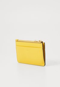 Portafoglio giallo in pelle con una superficie liscia, chiusura con zip nella parte superiore e più scomparti per carte su un lato. Design semplice e compatto.