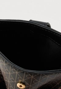 Μαύρη τσάντα χειρός με χρυσά μεταλλικά στοιχεία, που φέρει γεωμετρικό σχέδιο σε καφέ χρώμα. Το εσωτερικό έχει ματ μαύρο, λείο φινίρισμα.