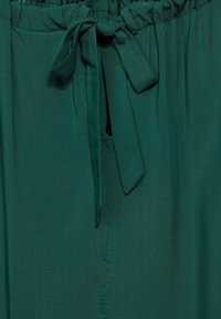 Abito di stoffa verde con vita elastica arricciata e cintura annodata. Presenta una leggera lucentezza e un logo sottile cucito di lato.